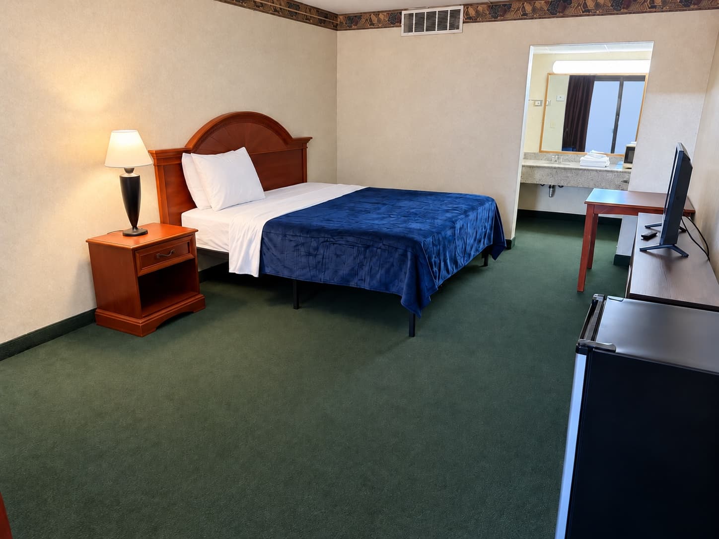 Guest room with a bed, nightstand, desk, and television